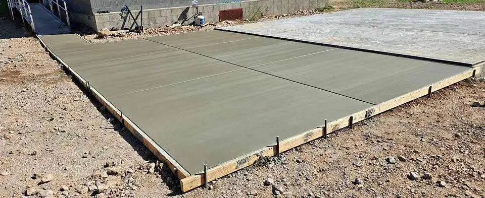 Freshly poured and smoothed, the concrete slab in Albuquerque, NM is expertly framed by wooden planks and surrounded by rough, rocky ground.