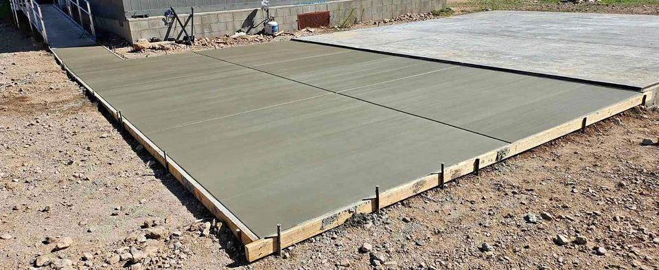 Freshly poured and smoothed, the concrete slab in Albuquerque, NM is expertly framed by wooden planks and surrounded by rough, rocky ground.