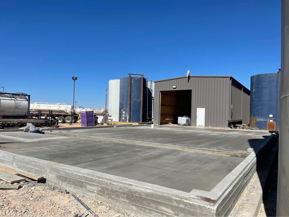 The image captures a large floor area under construction in Albuquerque, NM, lined with a grid of metal rebar for reinforcement. The Quality Concrete NM surface is unfinished, set against partially built walls and various construction materials from the commercial concrete contractor.